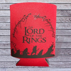 May include: Red can cooler with a black silhouette of the Lord of the Rings characters and the text "The Lord of the Rings" with the inscription "One Ring to rule them all" in black.