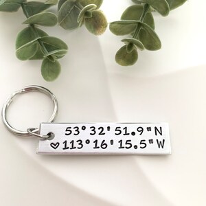 May include: Silver keyring with a rectangular tag engraved with the coordinates "53° 32' 51.9" N ♥ 113° 16' 15.5" W".