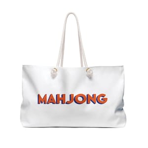Puede incluir: Bolsa de lona blanca con asas de cuerda y la palabra "MAHJONG" impresa en letras naranja y azul.