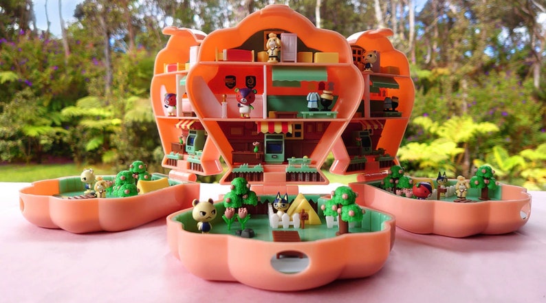 May include: A pink and green Animal Crossing-themed miniature dollhouse with multiple rooms and characters. The dollhouse is open to reveal the interior, which includes furniture, accessories, and characters. The dollhouse is made of plastic and has a whimsical design.
