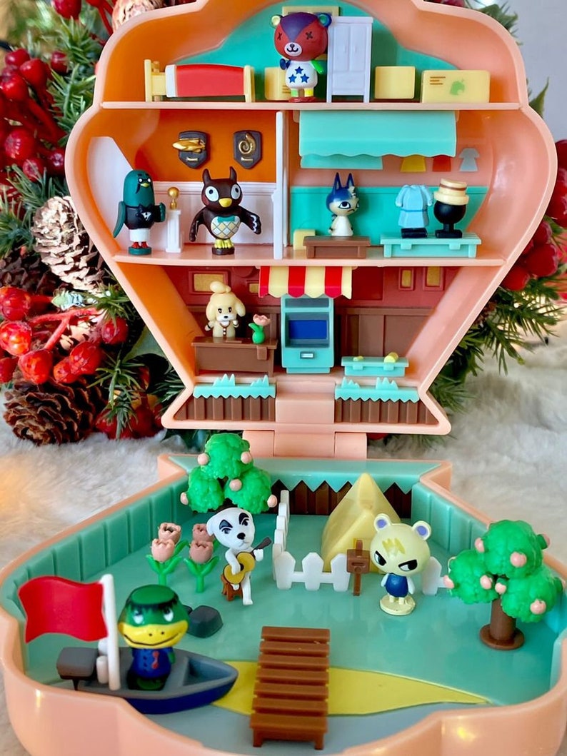 May include: A pink and blue plastic toy house with a green roof and a white picket fence. The house has a red flag, a brown wooden dock, and a yellow tent. There are several small plastic figures of animal characters from the Animal Crossing video game series.