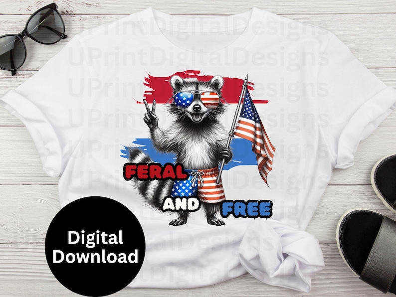 Puede incluir: Camiseta blanca con un mapache con gafas de sol con un dise&ntilde;o de la bandera estadounidense. El mapache sostiene una bandera estadounidense y lleva pantalones cortos rojos, blancos y azules. El texto de la camiseta dice "FERAL AND FREE".