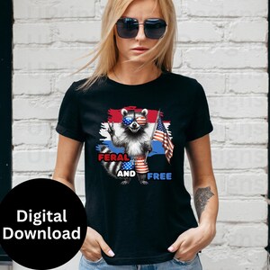 Puede incluir: Camiseta negra con un dise&ntilde;o de mapache con gafas de sol y ropa patri&oacute;tica, sosteniendo una bandera estadounidense. El texto "FERAL AND FREE" se muestra debajo. El dise&ntilde;o utiliza una combinaci&oacute;n de rojo, blanco y azul.