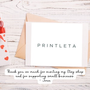 May include: A white card with the text "PRINTLETA" in green lettering. The card is on a wooden surface with a gift box wrapped in white paper with red hearts and a red ribbon.