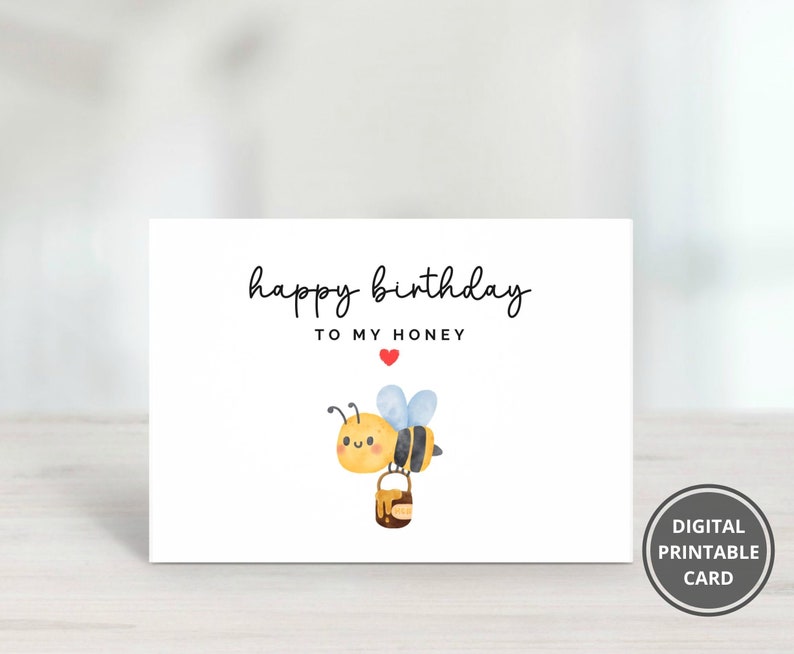 May include: A white printable birthday card with a cute cartoon bee carrying a pot of honey. The card says "happy birthday to my honey" with a red heart.