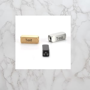 May include: Three metal objects with the word "Text" on them. One is gold, one is silver, and one is black. The objects are rectangular with rounded edges. The silver object has a hole in one end.