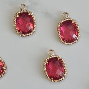 May include: A collection of ruby red gemstone pendants with gold-coloured twisted rope-like frames. Each pendant has a small loop at the top for attaching to a chain. The gemstones are faceted, and the pendants are scattered.