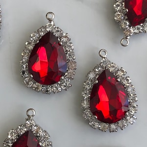 Peut inclure: Plusieurs pendentifs en strass rouges en forme de goutte d'eau avec des montures en métal argenté. Chaque pendentif présente une grosse pierre rouge facettée entourée de petits strass transparents. Les pendentifs ont une petite boucle en haut pour la fixation.