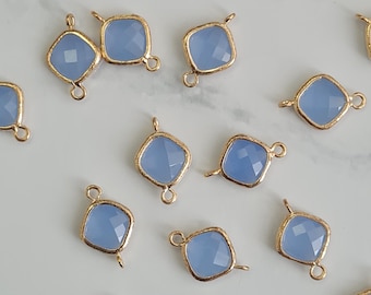Puede incluir: Una colección de colgantes de piedras preciosas de color azul claro, de forma cuadrada, con marcos de metal dorado. Cada colgante tiene un lazo en la parte superior e inferior para sujetarlo a la joyería. Las piedras preciosas tienen una superficie facetada.
