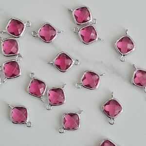 May include: A selection of magenta-coloured crystal pendants with silver metal frames. Each square-shaped pendant has a loop for attaching to jewellery. The faceted crystals catch the light, creating a sparkling effect. Ideal for jewellery making.