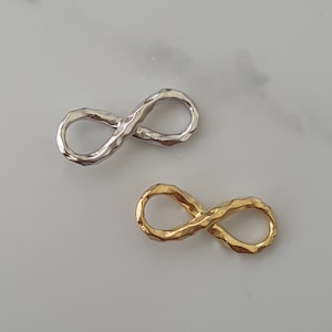 Peut inclure: Deux breloques en forme de symbole infini, l'une en argent et l'autre en or. Les deux breloques ont une finition texturée martelée.