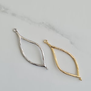 Peut inclure: Deux breloques en forme de feuille en métal, l'une argentée et l'autre dorée. Les deux breloques ont une surface texturée et une boucle en haut pour les attacher à des bijoux.