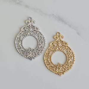 May include: Two ornate filigree pendants, one silver-toned and one gold-toned, with a circular center and intricate floral designs. Each pendant has a small loop at the top for hanging. The pendants are likely for jewelry making or crafting.