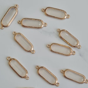 May include: A selection of rectangular jewellery components. Each component has a clear, rectangular centre within a gold-coloured metal frame. Small loops are on each end for attachment, suitable for jewellery making.