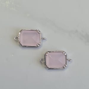 May include: Two rectangular, light pink gemstone connectors with silver-colored metal frames. Each connector has a loop on each side for attaching to other jewelry components. The gemstones have a faceted appearance.