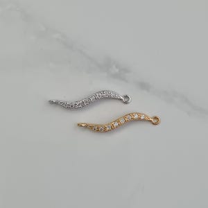 Peut inclure: Deux breloques de connecteur ondulées, argent et or, avec des pierres de zircone cubique transparentes.