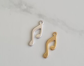Pode incluir: Dois pingentes em forma de nota musical, um prateado e outro dourado. Os pingentes têm a forma de uma clave de sol.