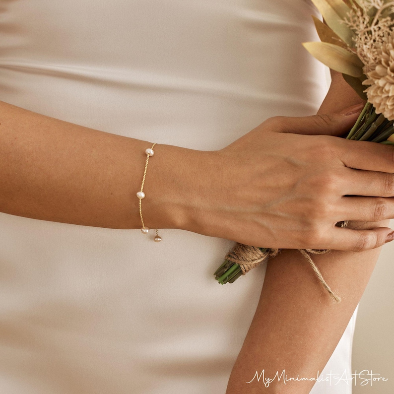 May include: A delicate gold chain bracelet with small pearl accents. The bracelet is adjustable and has a simple, minimalist design.