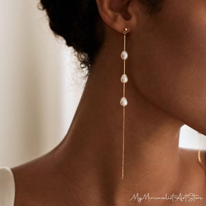 Puede incluir: Pendientes de cadena de oro con cuatro gotas de perlas blancas que cuelgan de la cadena. Los pendientes son largos y cuelgan hasta el cuello.