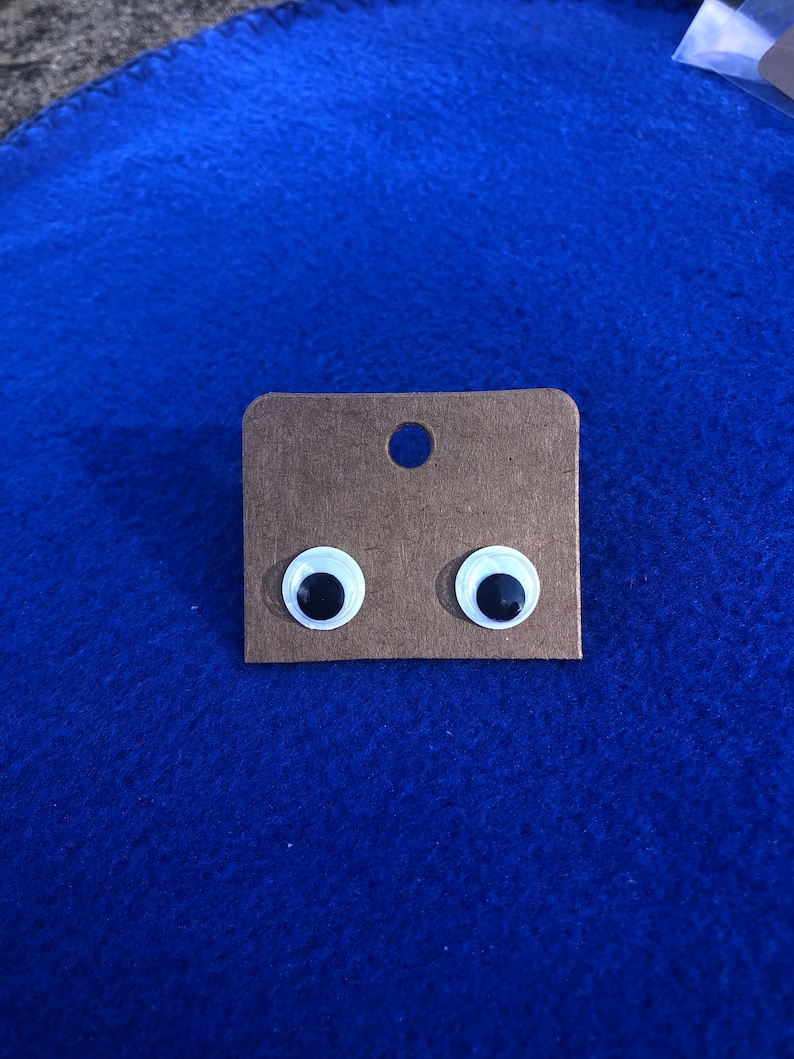May include: A pair of googly eyes on a brown card. The eyes are white with black pupils.