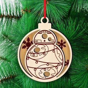 K&ouml;nnte beinhalten: Weihnachtsbaumschmuck aus Holz mit einem BB-8-Droiden-Design. Der runde Schmuck hat ein mehrschichtiges Design, das die Details des Droiden in Braun vor einem helleren Holzgrund zeigt. Inklusive rotem Band zum Aufh&auml;ngen. Festliche Weihnachtsdekoration.