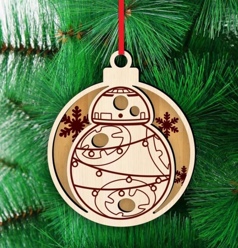 K&ouml;nnte beinhalten: Weihnachtsbaumschmuck aus Holz mit einem BB-8-Droiden-Design. Der runde Schmuck hat ein mehrschichtiges Design, das die Details des Droiden in Braun vor einem helleren Holzgrund zeigt. Inklusive rotem Band zum Aufh&auml;ngen. Festliche Weihnachtsdekoration.