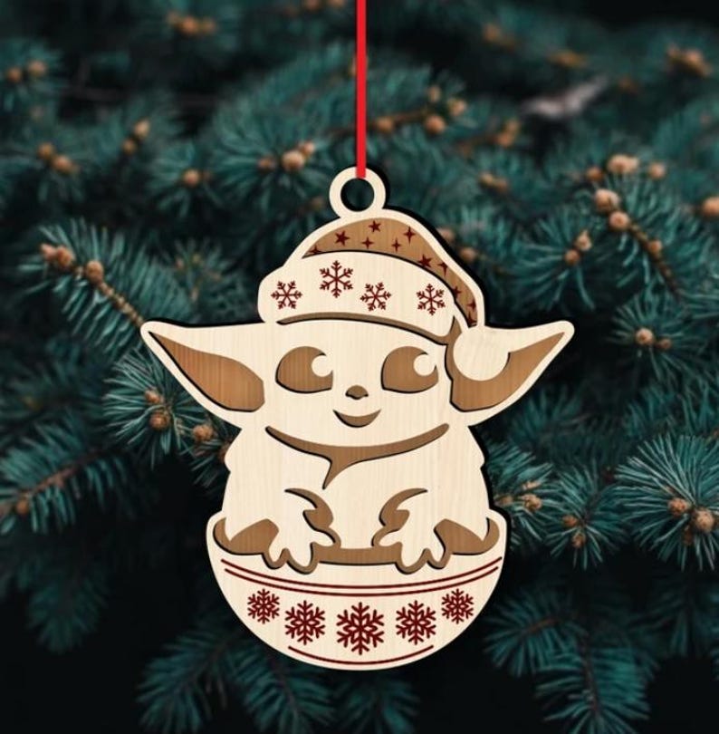 K&ouml;nnte beinhalten: Weihnachtsbaumschmuck aus Holz mit einer stilisierten Figur mit Weihnachtsm&uuml;tze und Schneeflockenmuster. Der Anh&auml;nger h&auml;ngt an einem roten Faden vor einem Hintergrund aus Tannenzweigen. Die Figur befindet sich in einer Sch&uuml;ssel mit Schneeflockendetails.