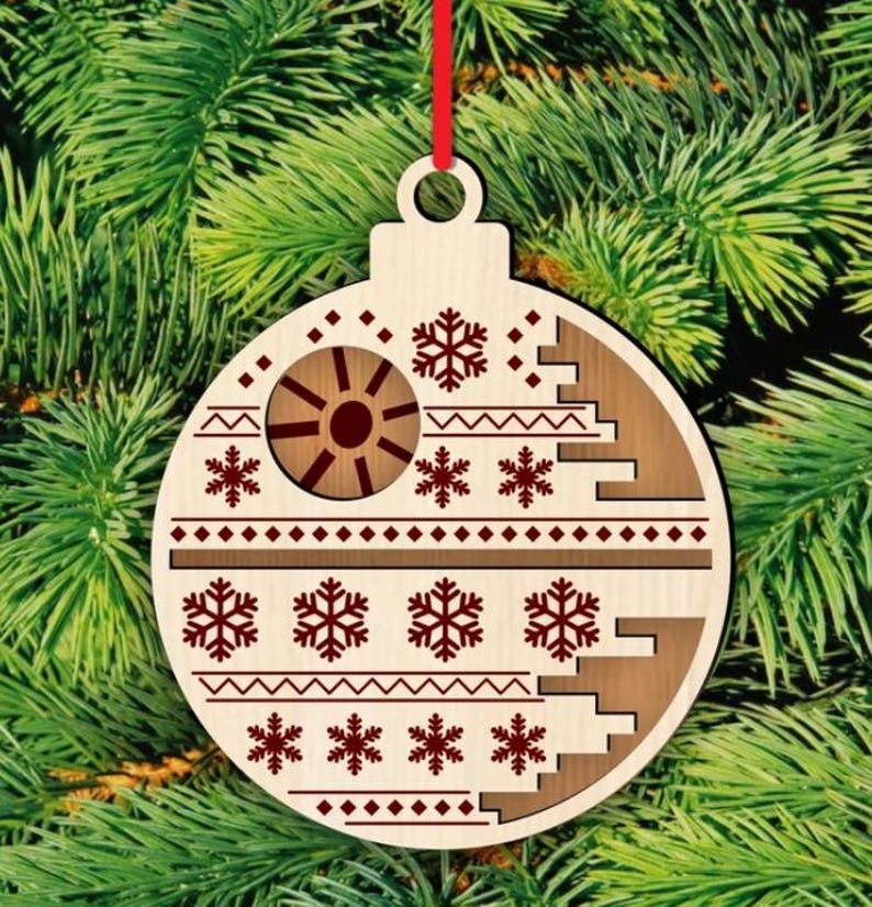 K&ouml;nnte beinhalten: Weihnachtsbaumschmuck aus Holz mit rotem Band. Der Schmuck ist hellbraun mit einem braunen Design mit Schneeflocken und einem kreisf&ouml;rmigen Design. Der Schmuck h&auml;ngt vor einem gr&uuml;nen Weihnachtsbaum.