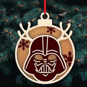 K&ouml;nnte beinhalten: Weihnachtsschmuck aus Holz mit Darth Vaders Helmdesign. Der Schmuck hat eine hellbraune Holzbasis mit einer dunkelroten Helmumrandung und Schneeflocken-Akzenten. Ein rotes Band ist zum Aufh&auml;ngen befestigt.