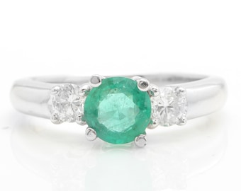 May include: A white gold ring featuring a large emerald gemstone flanked by two smaller round diamonds.