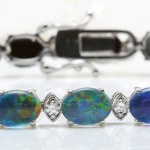Op de afbeelding: Een zilveren armband met een rij ovale blauwe opalen en kleine heldere diamanten. De armband heeft een sluiting.