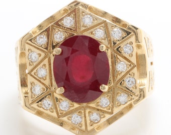 May include: A gold ring with a large red ruby gemstone surrounded by smaller white diamonds. The ring has a geometric design with a hexagonal shape.