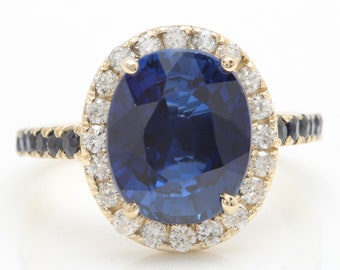 May include: A gold ring with a large oval blue sapphire surrounded by a halo of smaller diamonds. The band is set with smaller black sapphires.