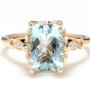 May include: A gold ring featuring a large, rectangular, light blue gemstone. The ring has small accent stones on either side of the main stone. The band is a simple, polished gold.