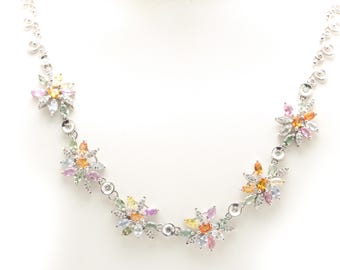 May include: A silver necklace with a delicate chain and colorful flower-shaped pendants. Each pendant is adorned with small, sparkling gemstones in shades of pink, yellow, blue, and green.
