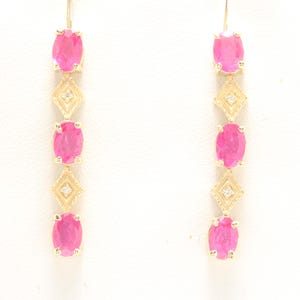 Peut inclure: Boucles d'oreilles pendantes avec une monture dorée. Chaque boucle d'oreille présente trois pierres précieuses roses vives de forme ovale et deux motifs en forme de losange avec de petites pierres claires. Les boucles d'oreilles pendent verticalement.