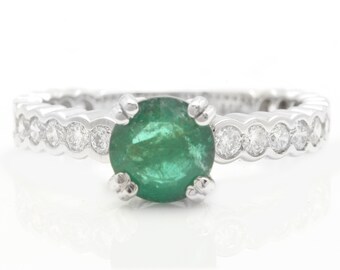 May include: A white gold ring featuring a round emerald gemstone set in a band of small diamonds.