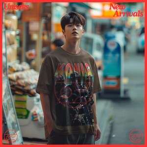 May include: A brown t-shirt with a graphic print of a group of people wearing military gear. The graphic has the word "KONICA" printed in a colorful font.