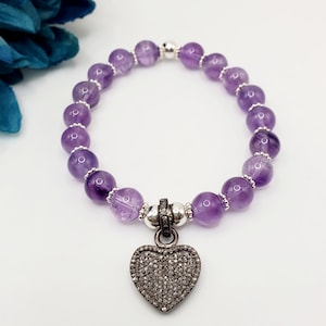 May include: A purple amethyst gemstone bracelet with a silver heart charm encrusted with small diamonds.