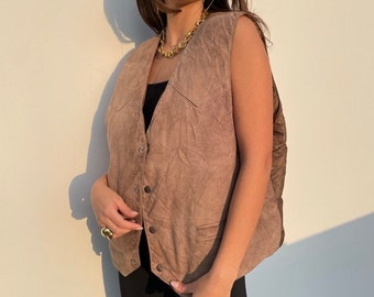 May include: A brown suede vest with a button-up front and a quilted lining. The vest has a classic western style with a pointed collar and flap pockets.