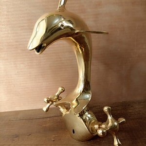May include: A gold-toned brass faucet shaped like a dolphin with two cross-shaped handles.