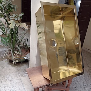 Pode incluir: Uma pia de cozinha de aço inoxidável de cor dourada com forma retangular. A pia está sobre uma mesa de madeira.