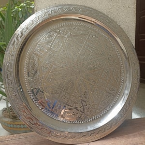 May include: A silver serving tray with an intricate geometric design. The tray has a raised rim and a smooth surface.
