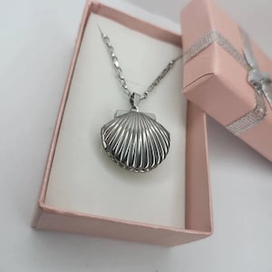 May include: A silver seashell locket necklace in a pink gift box. The locket is shaped like a seashell and has a detailed design.