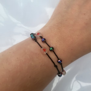 May include: A black string bracelet with iridescent beads and clear beads with red hearts.
