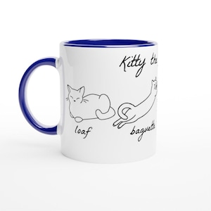 Puede incluir: Taza de cerámica blanca con interior y asa azules. La taza presenta dibujos lineales negros de gatos etiquetados como "loaf" y "baguette", con el texto "Kitty the". Una divertida taza con temática de gatos.