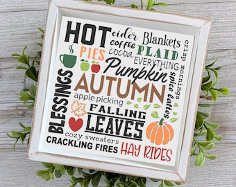 May include: A white wooden sign with a distressed finish featuring a fall-themed word art design. The words include "Hot", "Cider", "Blankets", "Blessings", "Pies", "Coffee", "Plaid", "Cocoa", "Everything", "Pumpkin", "Autumn", "Apple Picking", "Falling", "Leaves", "Cozy Sweaters", "Crackling Fires", "Hay Rides", and "Crisp Mornings".