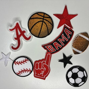 May include: A collection of embroidered patches featuring sports themes. Includes a basketball, football, baseball, soccer ball, stars, and a foam finger. The patches are in various colors, including red, white, black, and brown.