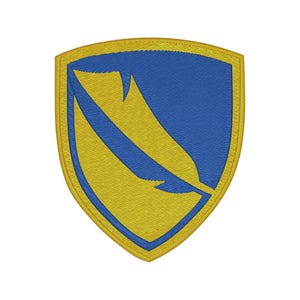 May include: A shield-shaped embroidered patch featuring a blue background with a diagonal yellow feather graphic. The patch is bordered by a thick yellow stitched edge, creating a distinct contrast between the blue and yellow colour scheme.