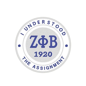 Può includere: Una toppa ricamata circolare con la scritta "I UNDERSTOOD THE ASSIGNMENT" in un bordo bianco. Il centro presenta le lettere "ZΦB" e il numero "1920" in blu.
